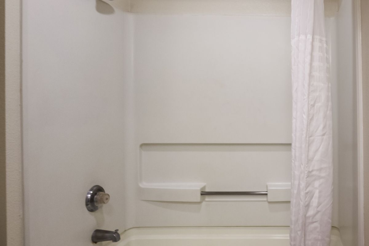 A bathroom with a white bathtub and shower, a curved shower rod with a white curtain, and a towel draped over the tub edge, is shown in the image.