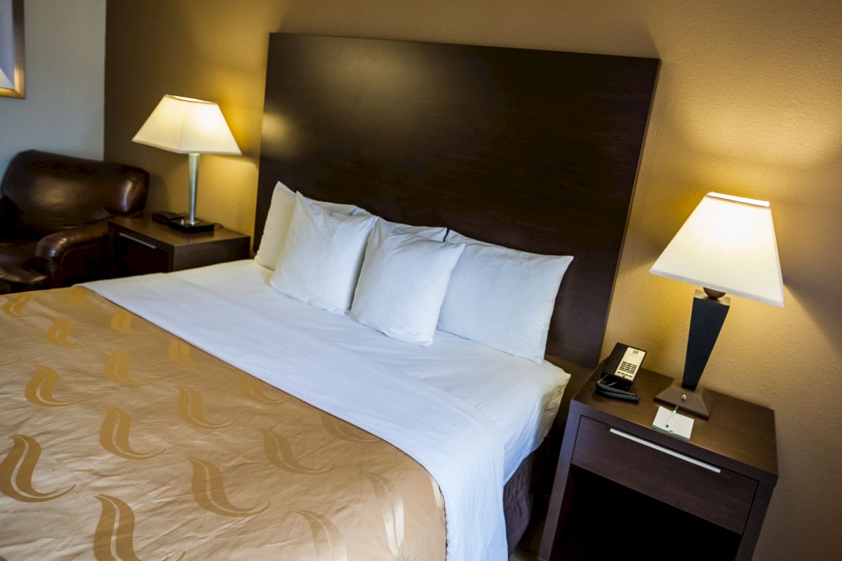 A neatly made bed with three pillows and two bedside tables with lamps in a cozy, dimly lit room.