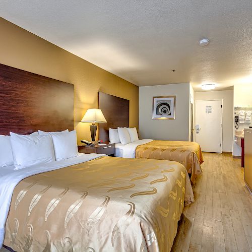 A hotel room with two double beds, a lamp between them, a TV on a dresser, and a bathroom door visible in the back.