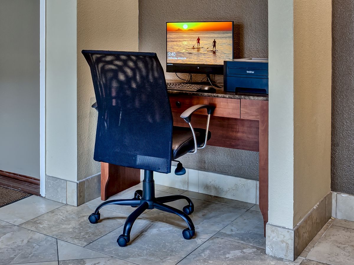 The image shows a small office nook with a chair, desk, computer, and printer, with a beach scene screensaver on the monitor.