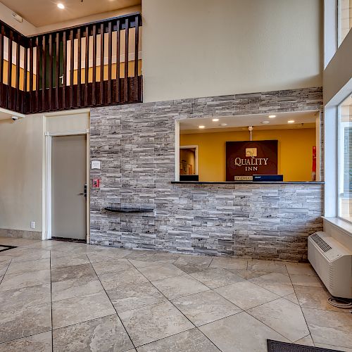 The image shows a hotel lobby with a reception desk labeled "Quality Inn," a brochure stand, tiled flooring, and a second-floor balcony area.