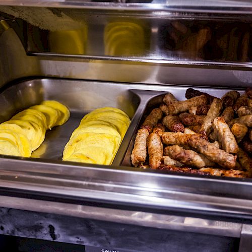 The image shows a heated buffet tray with a section of cooked sausages and another section containing sliced eggs.