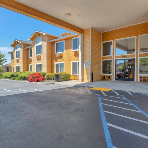 The image shows the entrance of a two-story building with parking spaces and a covered driveway.