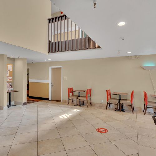 This image shows a spacious lobby area with tiled flooring, tables, and red chairs. There's also a snack machine on the left side.