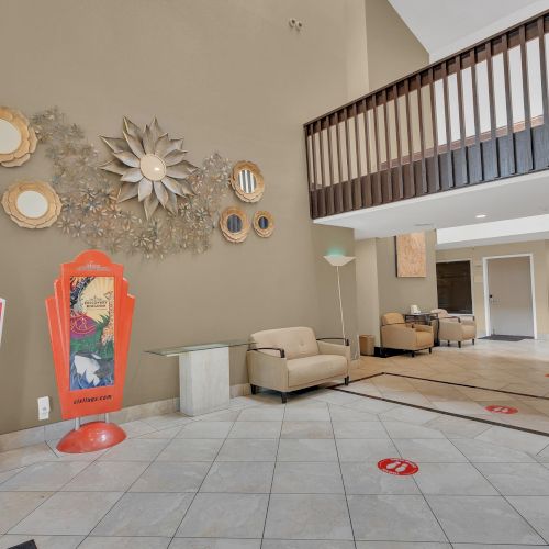The image shows a lobby with modern decor, signage, sofas, a second-floor railing, and wall art, creating a welcoming atmosphere.