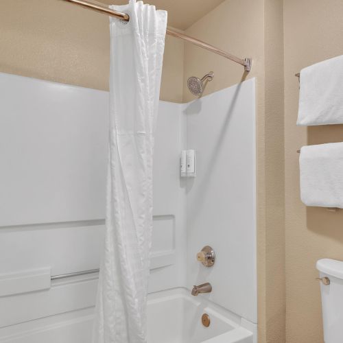 The image shows a bathroom with a white bathtub and shower, a curtain, and neatly folded towels on a wall rack.
