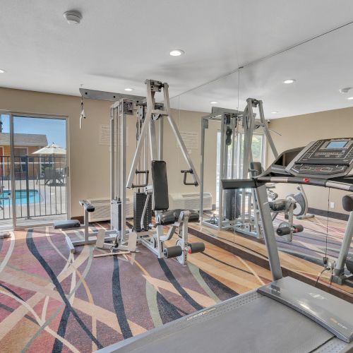 The image shows a gym room with exercise equipment, including a treadmill and weight machine, with a large mirror on one wall.
