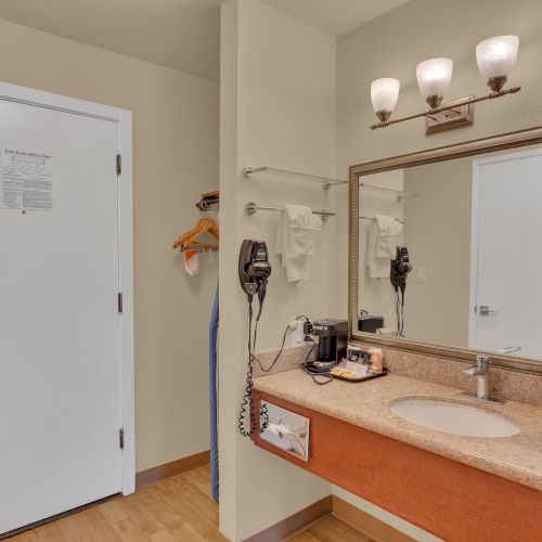A hotel room entryway features a sink, mirror, hairdryer, coffee maker, and closet area with hangers.