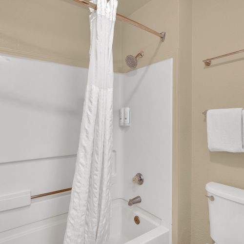 The image shows a bathroom with a bathtub, a shower curtain, a toilet, and towels on a rack on the wall.