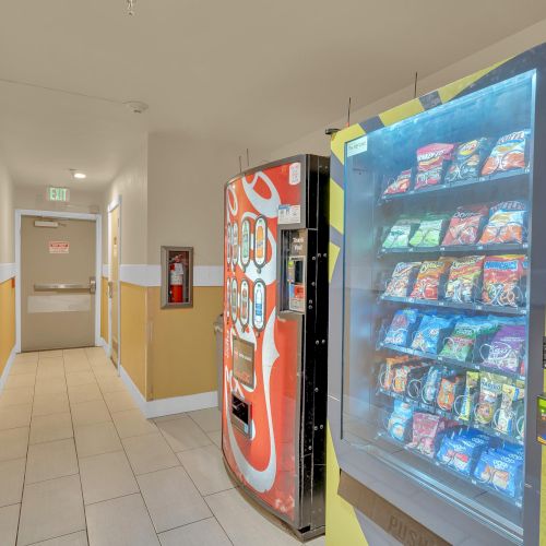 A hallway with two vending machines, one for drinks and another for snacks, and a door at the end.