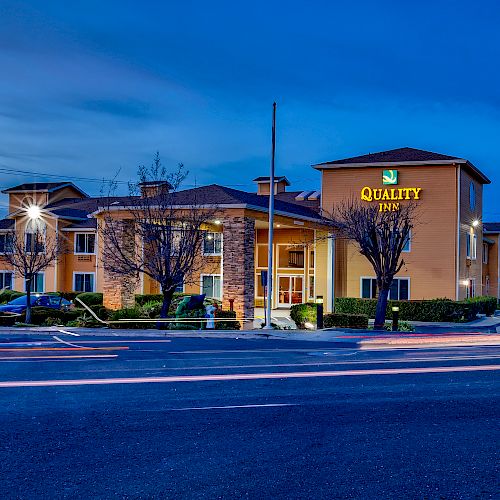 The image shows a "Quality Inn" building at dusk, with illuminated signs on the exterior and light trails from passing vehicles on the road in front.