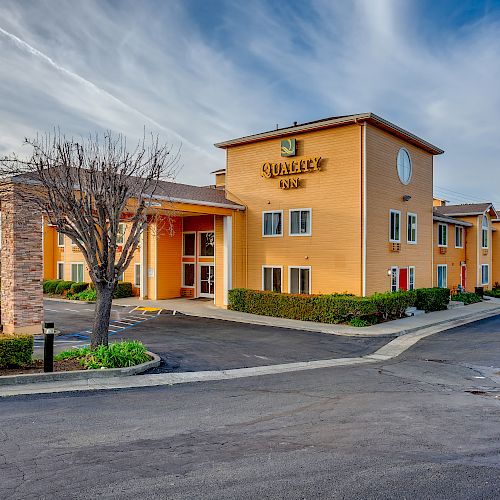 The image shows the exterior of a two-story hotel named "Quality Inn," featuring a porte-cochere, well-maintained landscaping, and a spacious parking lot.