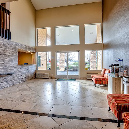 The image shows a spacious, modern lobby with tiled flooring, seating, a reception desk, a coffee station, and large windows letting in ample light.