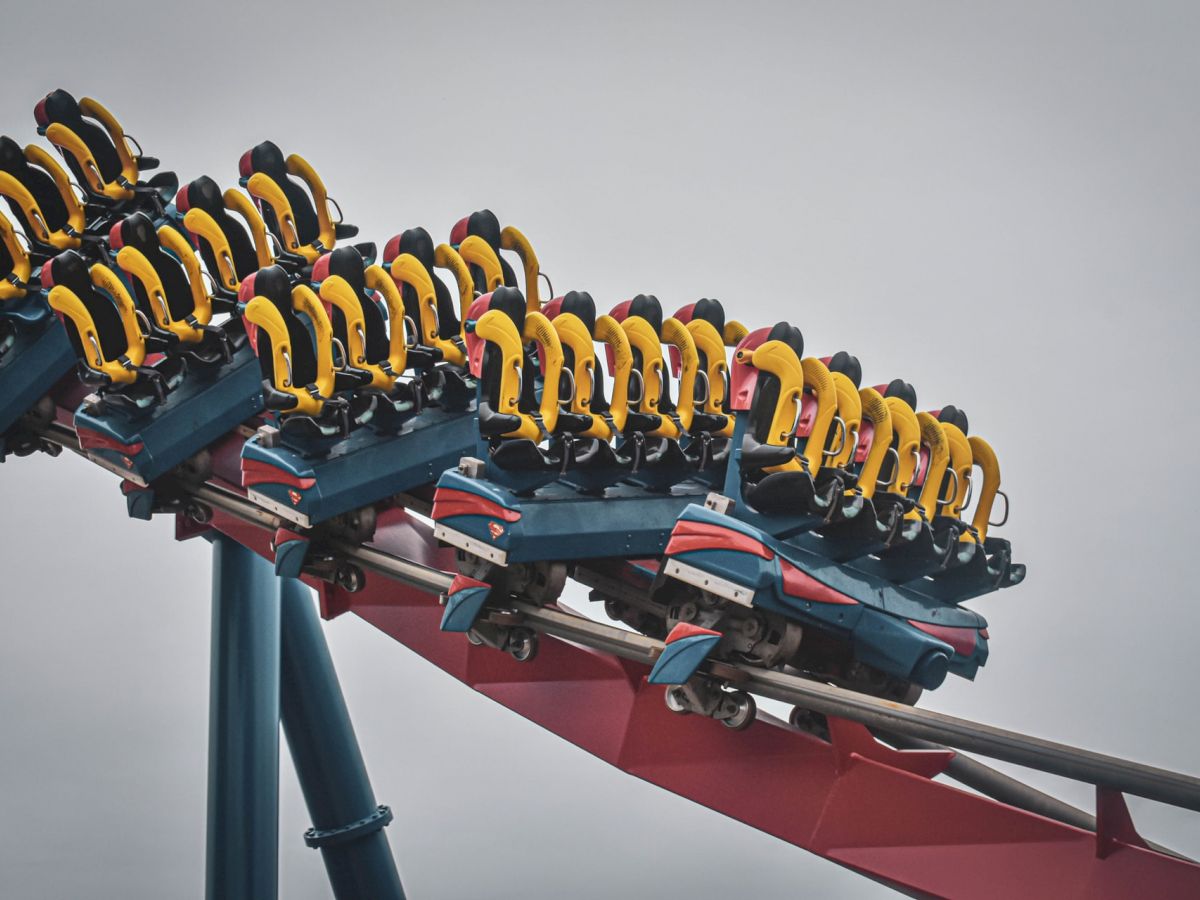 The image shows a section of a roller coaster with multiple yellow and red seats, as well as a curved red track against a gray sky.