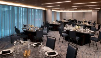 A nicely set up banquet hall with round tables and chairs, adorned with elegant table settings, flowers, and cutlery, ready for an event.