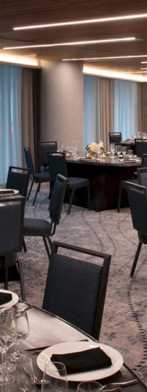 A banquet hall with round tables set for an event, featuring black chairs, elegant table settings with napkins, glassware, floral centerpieces, and candles.