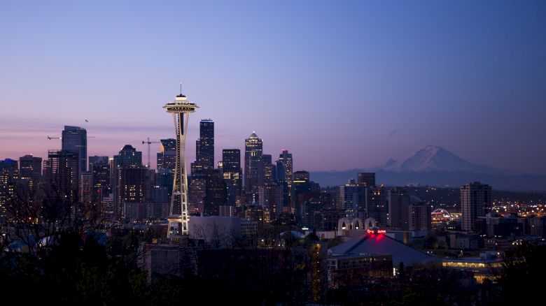 The image shows a city skyline at dusk with a prominent tower, several skyscrapers, and a mountain in the background.