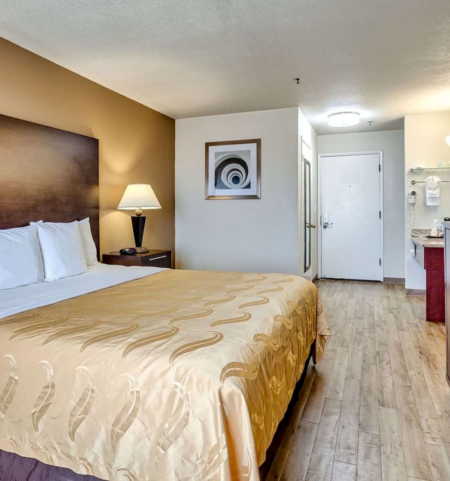 The image shows a tidy hotel room with a queen-sized bed, TV, microwave, nightstand, and an open door leading to a bathroom.