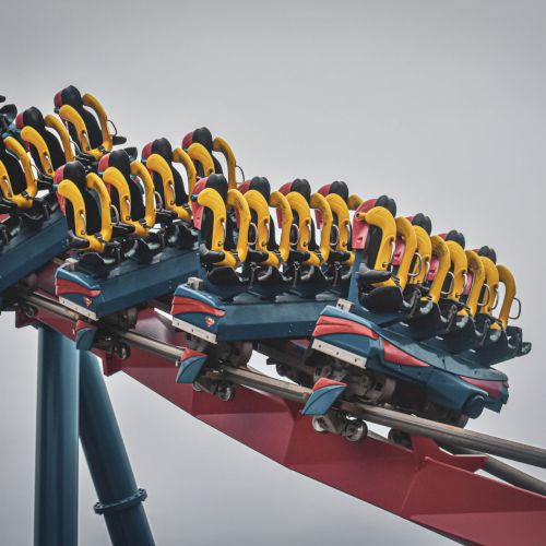 A roller coaster with empty yellow-seated cars making a turn on a red track against a cloudy sky background.