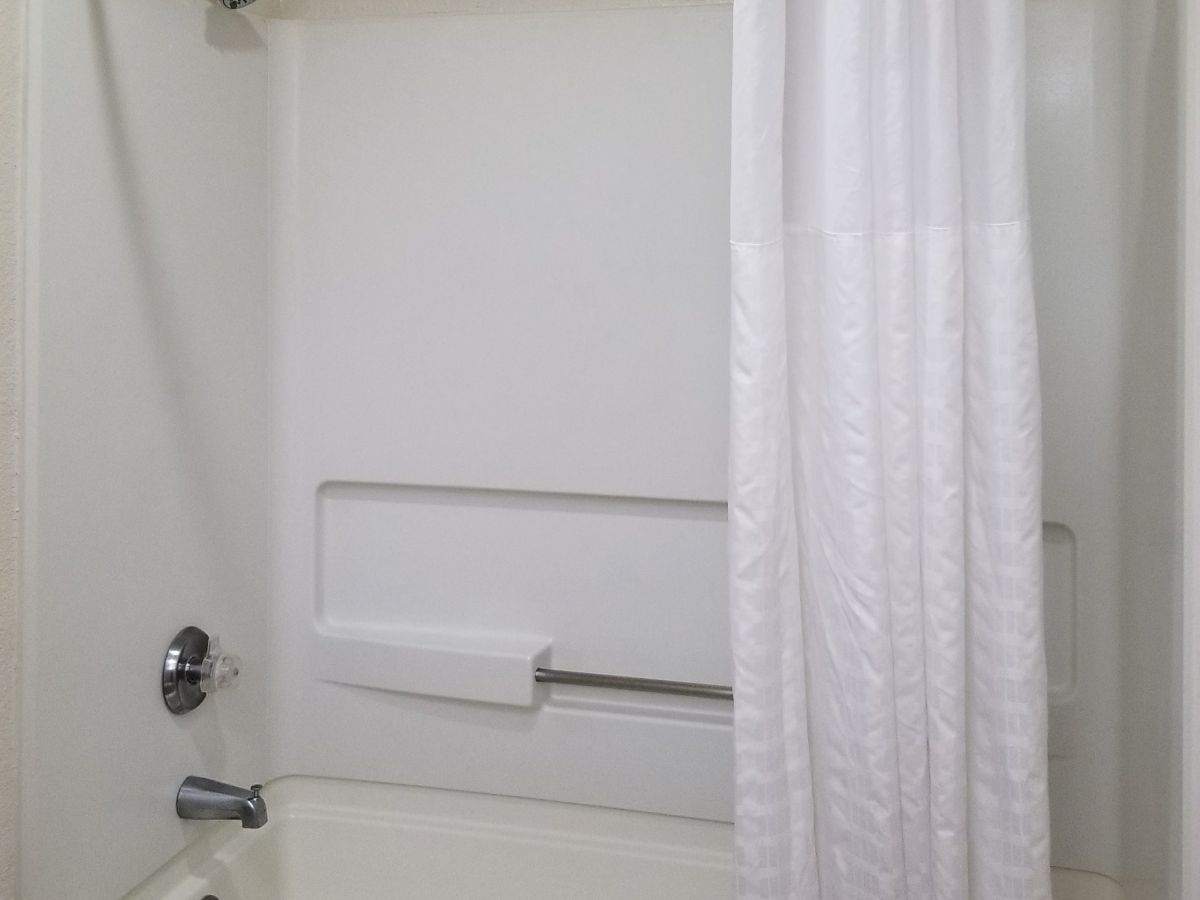 This image shows a white bathroom with a shower-tub combination, a shower curtain, a soap holder, and a white towel hanging over the tub edge.